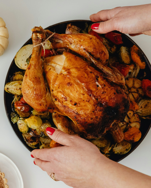 Roasted chicken with vegetables on a plate, hands serving