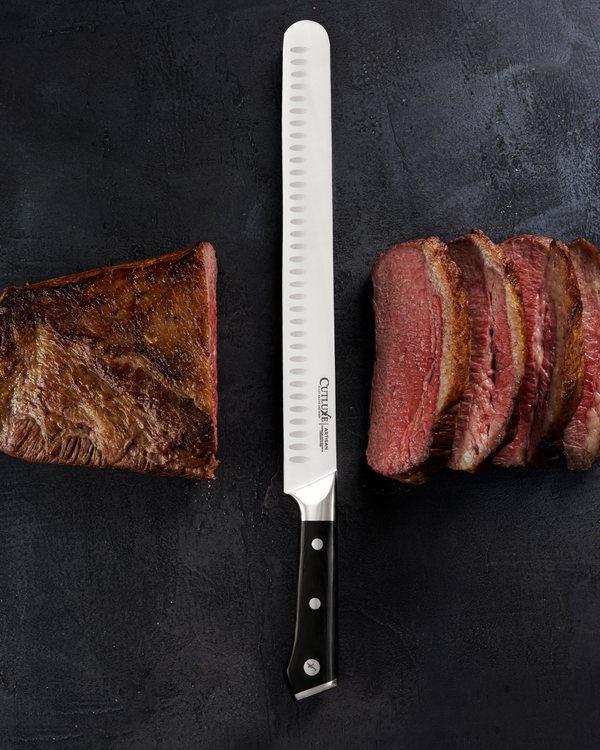 Serrated knife slicing medium-rare steak on dark surface