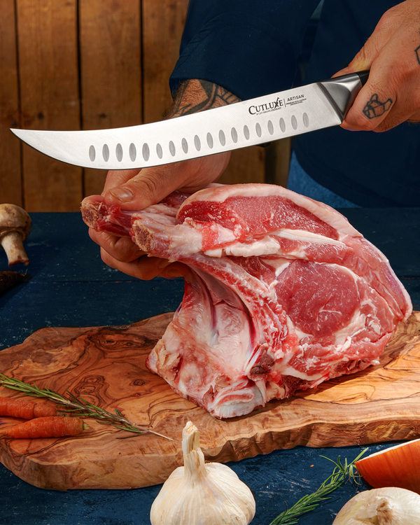 Sharp kitchen knife slicing raw meat on wooden cutting board with herbs and garlic