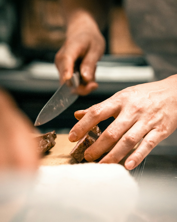 Chef slicing steak with sharp kitchen knife on wooden cutting board