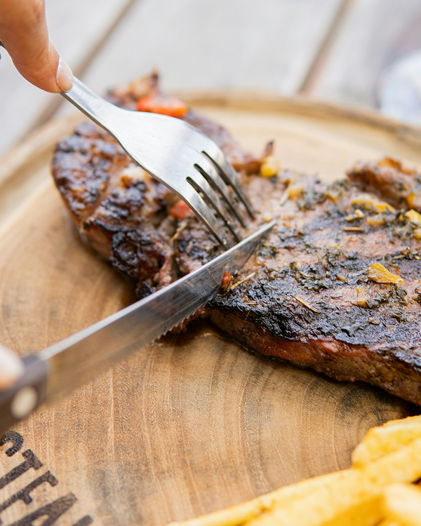 Slicing grilled steak with sharp kitchen knife and fork on wooden board